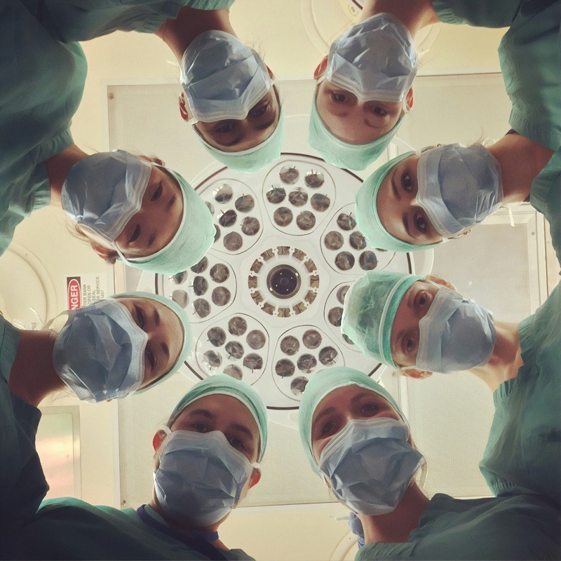 A patient's view from the exam table, a ring of masked clinicians looking down