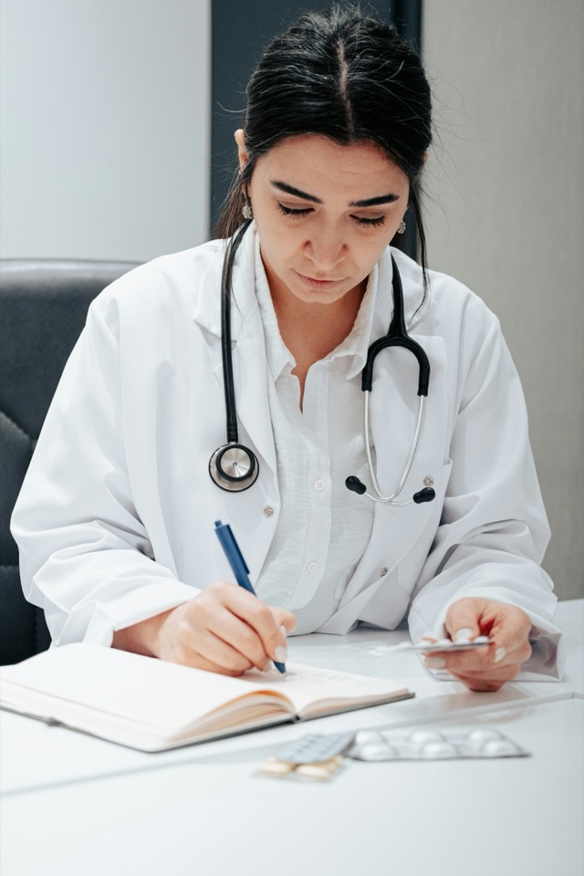 A physician in a white coat writing notes at a desk